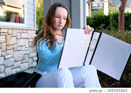 teenage girl leafing through notebook holding pencil learning to sit on street school desire to study excellent student correct child blue blouse loose hair 12-15 years old space for advertising text 109395865