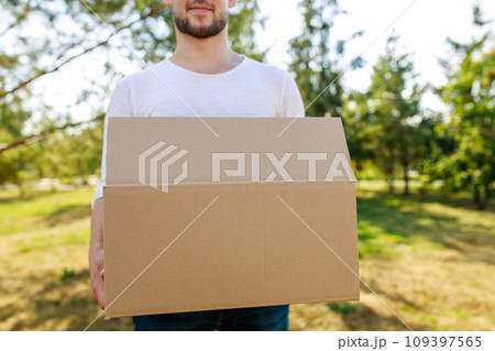 Man in white blazer holding cardboard boxes outdoor in summer park 109397565
