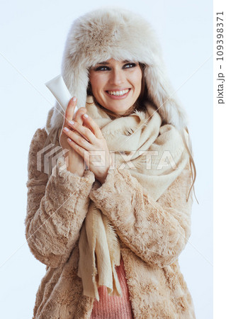 smiling modern woman in winter coat and fur hat on white 109398371