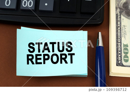 On a brown surface lies a calculator, dollars, pens and stickers with the inscription - STATUS REPORT On a brown surface lies a calculator, dollars, pens and stickers with the inscription - STATUS REPORT 109398712