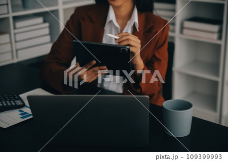 Attractive smiling young asian business woman work at home office, Asian woman working on laptop computer holding tablet. 109399993