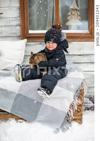 A little boy sits in the snow and holds a cat A little boy sits in the snow and holds a cat 109401043