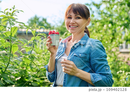 Happy woman in raspberry bushes garden, with cup ripe raspberries 109402128