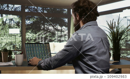 Self employed banker following stock exchange trends from his extravagant luxurious cabin inside the forest, opening laptop to see investment updates. Entrepreneur living in rich mountain villa. 109402983