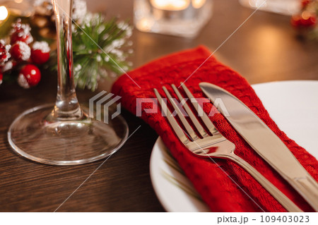 Christmas table setting. Plate and cutlery on napkin. Preparing for festive dinner. Candles burning on table on Christmas Eve. 109403023