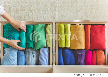 Women's hands take bright rainbow clothes from a wardrobe drawer. The concept of order and storage Women's hands take bright rainbow clothes from a wardrobe drawer. The concept of order and storage 109403450