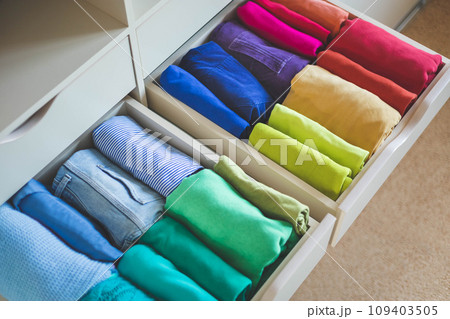 A lot of colorful clothes are neatly arranged in a wardrobe drawer. The concept of storage. A lot of colorful clothes are neatly arranged in a wardrobe drawer. The concept of storage. 109403505