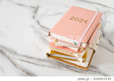 Pink coral colored diary for the year 2024 and many other diaries, pen, marble background 109403549
