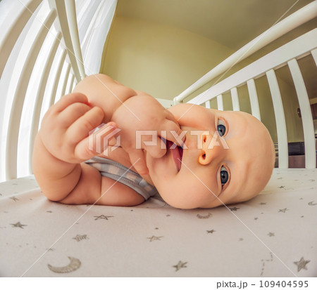 A playful baby in the crib, gleefully staring at the camera, radiating joy A playful baby in the crib, gleefully staring at the camera, radiating joy 109404595