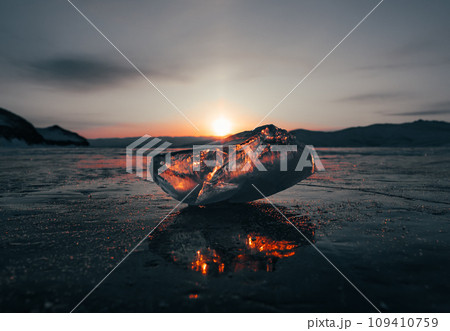 Ice crystal on the frozen surface of Lake Baikal in early morning. Sky and sun reflections on the ice surface. Amazing winter landscape. Winter tourist season at lake Baikal 109410759