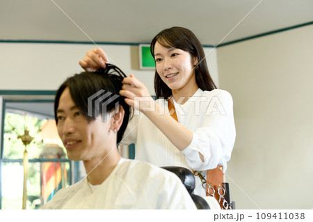 男性客のヘアスタイリングをするアジア人の女性美容師 男性客のヘアスタイリングをするアジア人の女性美容師 109411038