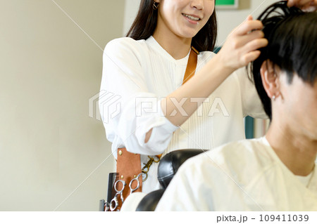 男性客のヘアスタイリングをするアジア人の女性美容師 男性客のヘアスタイリングをするアジア人の女性美容師 109411039