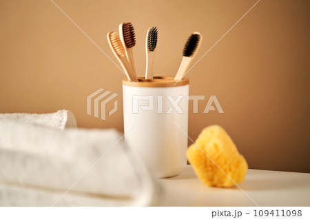 Bamboo toothbrushes in a cup and a towel in a bathroom interior. 109411098