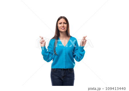 young beautiful European brunette woman dressed in a blue cardigan crossed her fingers in young beautiful European brunette woman dressed in a blue cardigan crossed her fingers in 109413440