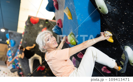 Mature female fitness climber training at bouldering gym.Woman rise up on artificial climbing wall 109413471