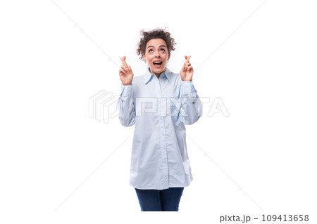 pretty young curly business woman in blue shirt crossed fingers on white background with copy space 109413658