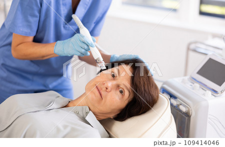 Aged woman undergoing cosmetic facial treatment using ion bubble attachment Aged woman undergoing cosmetic facial treatment using ion bubble attachment 109414046