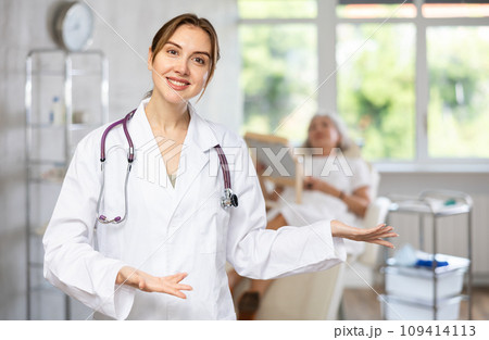 Smiling senior woman doctor in uniform with woman patient lying behind in clinic. Smiling senior woman doctor in uniform with woman patient lying behind in clinic. 109414113