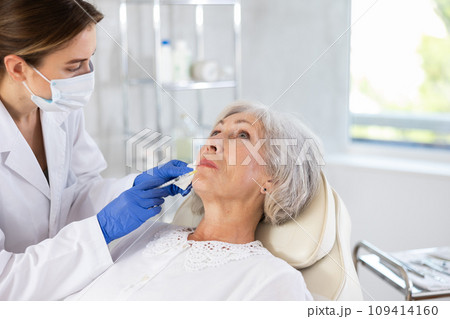 Eldery woman is getting a rejuvenating facial injections. She is lying calmly at clinic. 109414160