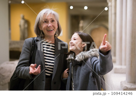 Elderly female tutor showing tween girl ancient sculptures in museum 109414246