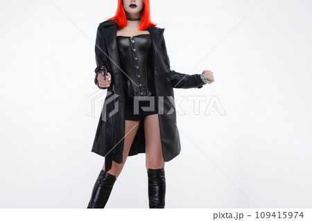 Young beautiful woman in a black leather corset and cloak with a gun in her hand on a white background Young beautiful woman in a black leather corset and cloak with a gun in her hand on a white background 109415974
