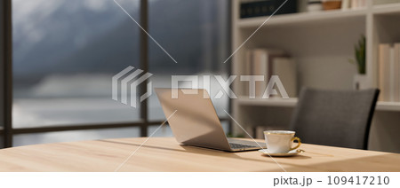 Close-up image of a laptop and a coffee cup on a wooden desk in a modern, luxury CEO office room. Close-up image of a laptop and a coffee cup on a wooden desk in a modern, luxury CEO office room. 109417210