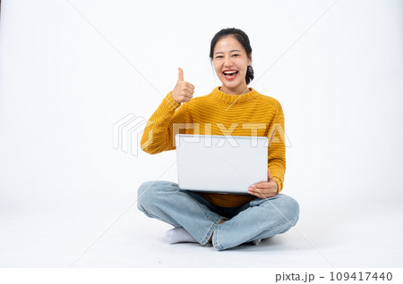 Happy woman sits on the floor on an isolated white background with her laptop and showing thumb up. Happy woman sits on the floor on an isolated white background with her laptop and showing thumb up. 109417440