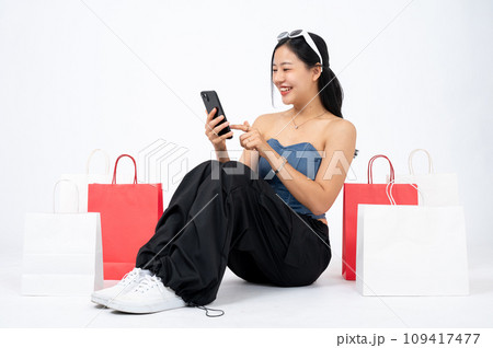 Elegant and happy Asian woman is enjoying shopping online on her smartphone, isolated background. 109417477