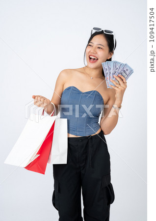 Elegant Asian woman in trendy clothes holding shopping bags and cash on an isolated white background Elegant Asian woman in trendy clothes holding shopping bags and cash on an isolated white background 109417504