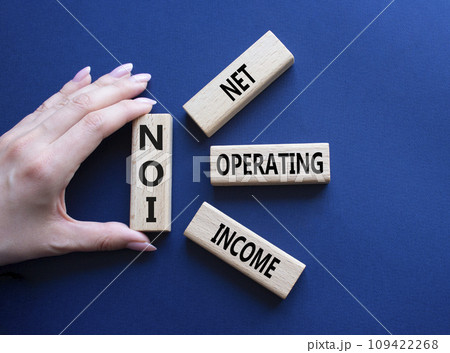NOI - Net Operating Income symbol. Concept word NOI on wooden cubes. Businessman hand. Beautiful deep blue background. Business and NOI concept. Copy space. 109422268