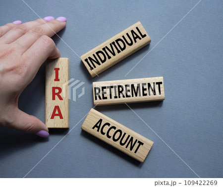 IRA - Individual Retirement Account symbol. Concept word IRA on wooden blocks. Businessman hand. Beautiful grey background. Business and IRA concept. Copy space. 109422269