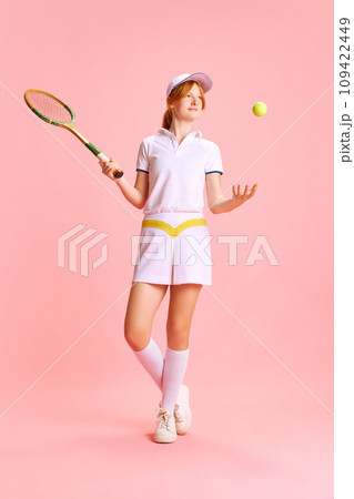 Full-length portrait of confident, beautiful woman, tennis player tosses ball with one hand against pastel pink background 109422449