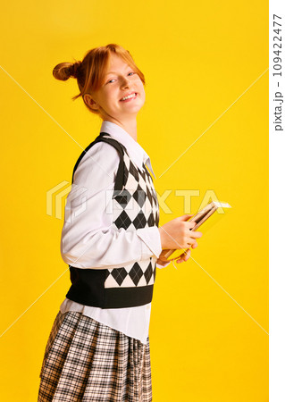 Side view portrait of adorable, cheerful smiling girl, student holds new just bought book against yellow background. Side view portrait of adorable, cheerful smiling girl, student holds new just bought book against yellow background. 109422477