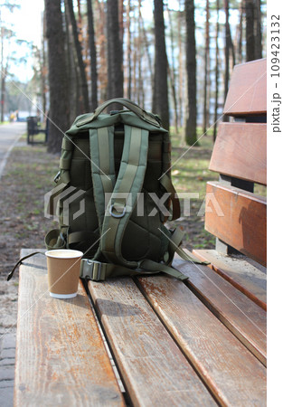 A travel bag with straps covers a paper cup of coffee from the wind on a bench in the park 109423132
