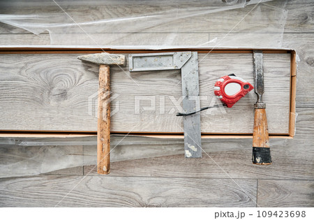 Metal construction ruler, hammer and measuring tape on laminate wood plank. Building repair tools and instruments for laminate flooring installation, construction works and home renovation. 109423698