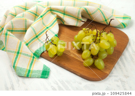 Cutting board with bunch of organic green grapes on white wooden background.. Cutting board with bunch of organic green grapes on white wooden background.. 109425844