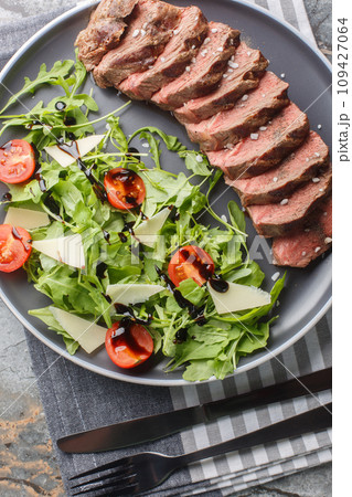 Beef tagliata with arugula, parmesan and cherry tomatoes is a delicious main course made with beef entrecote close-up on a plate. Vertical top view Beef tagliata with arugula, parmesan and cherry tomatoes is a delicious main course made with beef entrecote close-up on a plate. Vertical top view 109427064