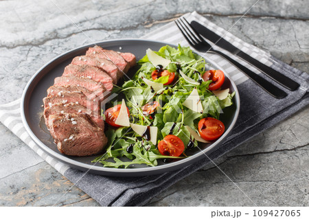 Beef steak tagliata with arugula, parmesan,  cherry tomatoes and balsamic close-up on a plate. Horizontal 109427065