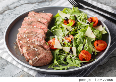 Traditional Italian main dish Beef tagliata tender steak, arugula, cherry tomatoes, Grana Padano shavings, balsamic reduction close-up on a plate on the table. Horizontal 109427066