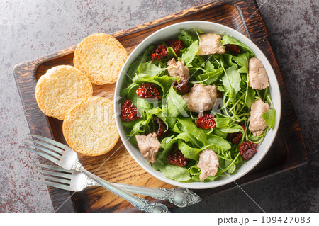 Canned cod liver salad with fresh arugula and sun-dried tomatoes served with toast close-up in a bowl. Horizontal top view Canned cod liver salad with fresh arugula and sun-dried tomatoes served with toast close-up in a bowl. Horizontal top view 109427083