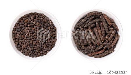 Dried black peppercorns and long pepper catkins, in white bowls. Berries of Piper nigrum, and fruits of Piper longum, sometimes called pippali. Used as spice and seasoning, both with similar taste. 109428584
