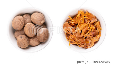 Dried true nutmegs and mace in white bowls. Whole seeds of Myristica fragrans, and the seed coverings of nutmeg seeds with yellow and orange tan. Used to flavor food and in preserving and pickeling. Dried true nutmegs and mace in white bowls. Whole seeds of Myristica fragrans, and the seed coverings of nutmeg seeds with yellow and orange tan. Used to flavor food and in preserving and pickeling. 109428585