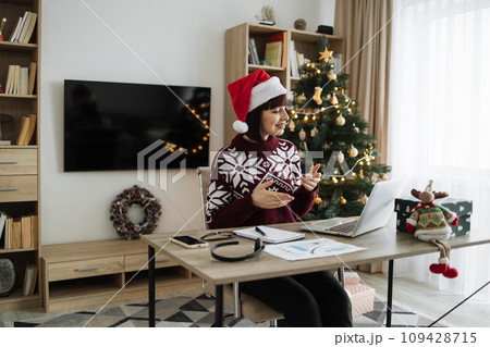 Female professional in Santa hat talking to client over video call on Christmas. Female professional in Santa hat talking to client over video call on Christmas. 109428715