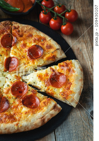 A slice of hot Italian pizza with stretching cheese. Pizza pepperoni on a dark wooden background A slice of hot Italian pizza with stretching cheese. Pizza pepperoni on a dark wooden background 109430107