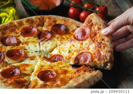 A slice of hot Italian pizza with stretching cheese. Pizza pepperoni on a dark wooden background 109430111