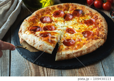 A slice of hot Italian pizza with stretching cheese. Pizza pepperoni on a dark wooden background A slice of hot Italian pizza with stretching cheese. Pizza pepperoni on a dark wooden background 109430113