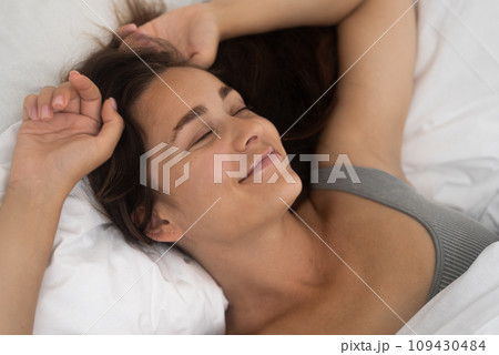 Sunrise Happiness: Greeting the new day with enthusiasm, a woman stretches in bed, embracing the morning's warmth with a contented grin.  109430484
