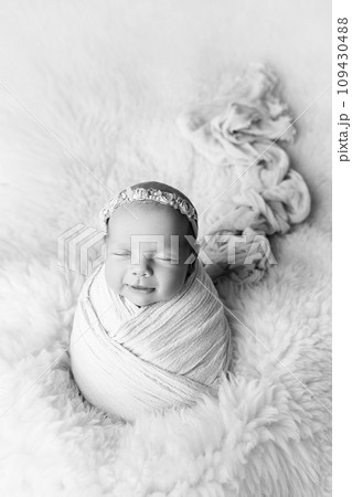 Sleeping newborn girl in the first days of life in a white cocoon with a white bandage on a white background. Studio macro photography, portrait of a newborn. The concept happiness. Black and white. Sleeping newborn girl in the first days of life in a white cocoon with a white bandage on a white background. Studio macro photography, portrait of a newborn. The concept happiness. Black and white. 109430488