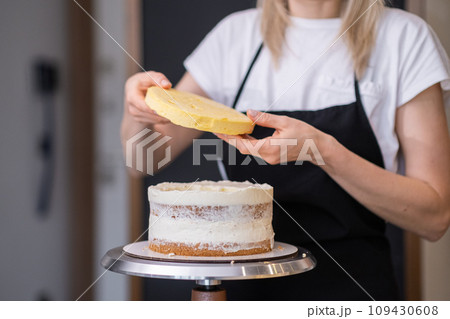 Professional confectioner in black apron connecting gluten free cake layers smeared with white cream skilled blonde woman working on handmade wedding pastry for client Professional confectioner in black apron connecting gluten free cake layers smeared with white cream skilled blonde woman working on handmade wedding pastry for client 109430608