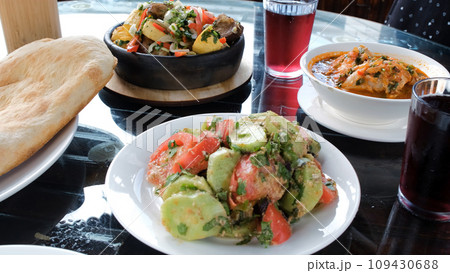 Close-up of various traditional tasty Georgian dishes on a table in cafe or a restaurant. Vegetable walnut sauce salad, ojahuri, chakhokhbili, freshly baked pitta bread and grape lemonade Close-up of various traditional tasty Georgian dishes on a table in cafe or a restaurant. Vegetable walnut sauce salad, ojahuri, chakhokhbili, freshly baked pitta bread and grape lemonade 109430688